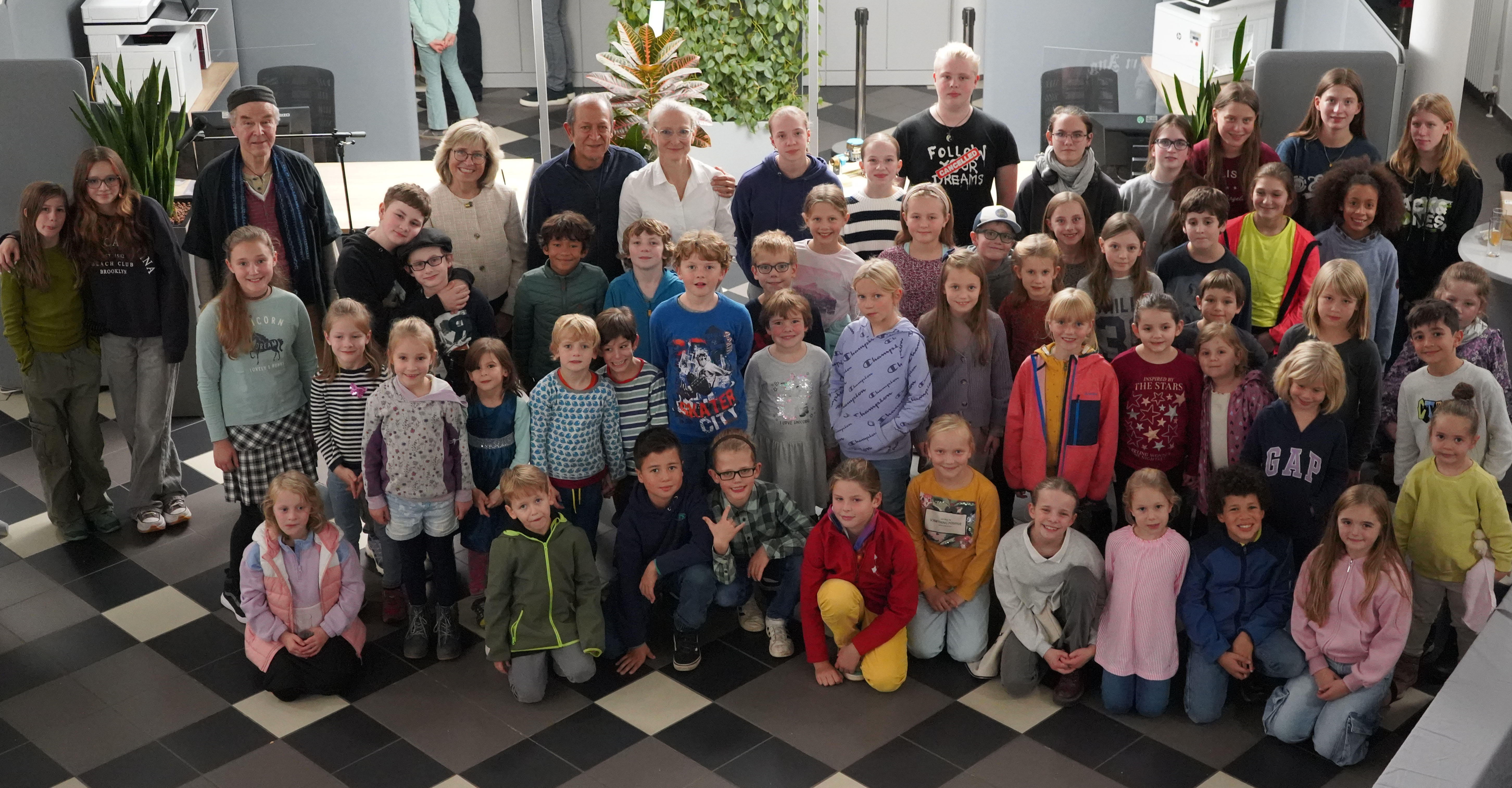 Gruppenbild von zahlreichen Kindern und Jugendlichen der Sommerkunstschule 2024 gemeinsam mit der Schauspieler und professionelle Geschichtenerzähler Peter Glass, Stadtwerke-Geschäftsführerin Andrea Vogt sowie Masoud Sadedin und Jette Jertz von der Troisdorfer KreativWerkstatt im Kundenzentrum des Lokalversorgers. ünst-lern der diesjährigen Sommerkunstschule, um gemeinsam das Finale der Ausstellung „Glück hat viele Farben“ in der Stadtwerke-Galerie zu feiern. 