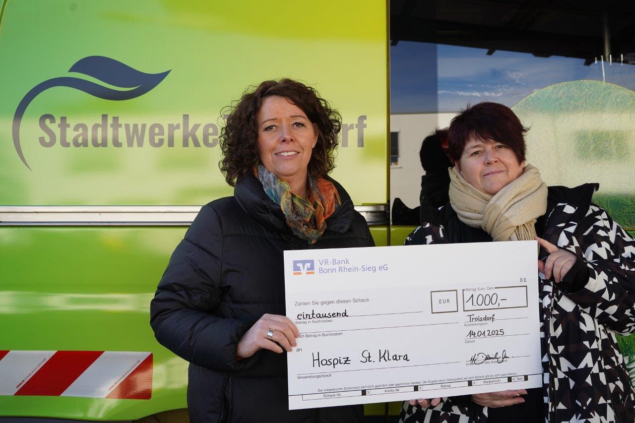 Zwei Frauen stehen mit einem Spendenscheck vor einem Stadtwerke-Auto 