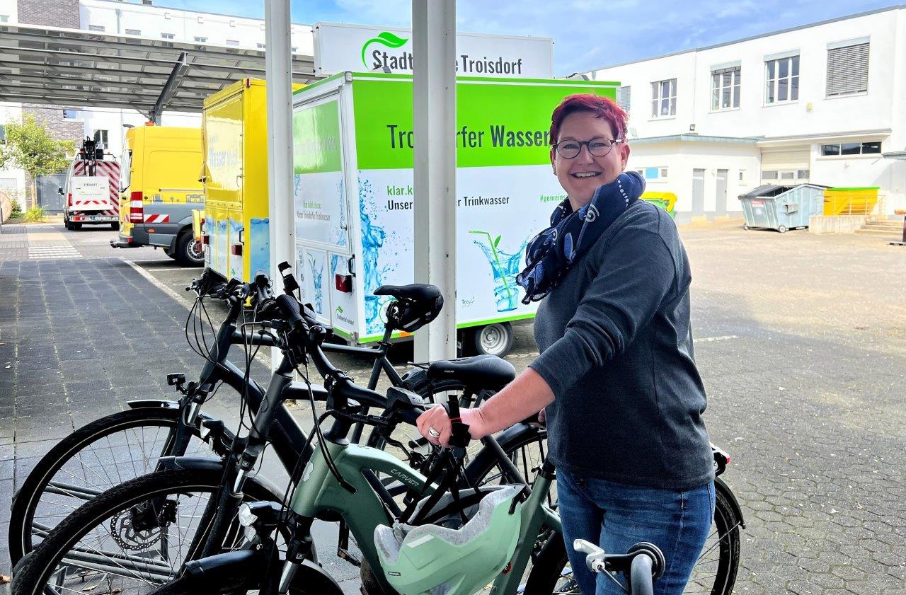 Mitarbeiterin steht auf dem Betriebshof an ihrem Fahrrad und schaut in die Kamera